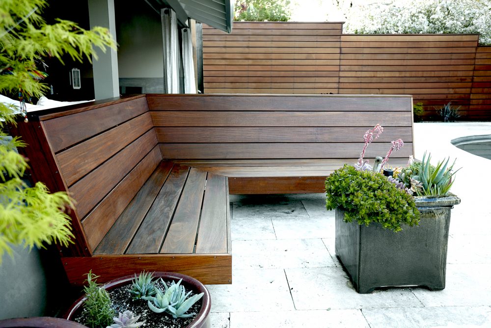 Dark polished, L shaped, built-in bench in the backyard next to the house with four wood boards as the back and four for the seat