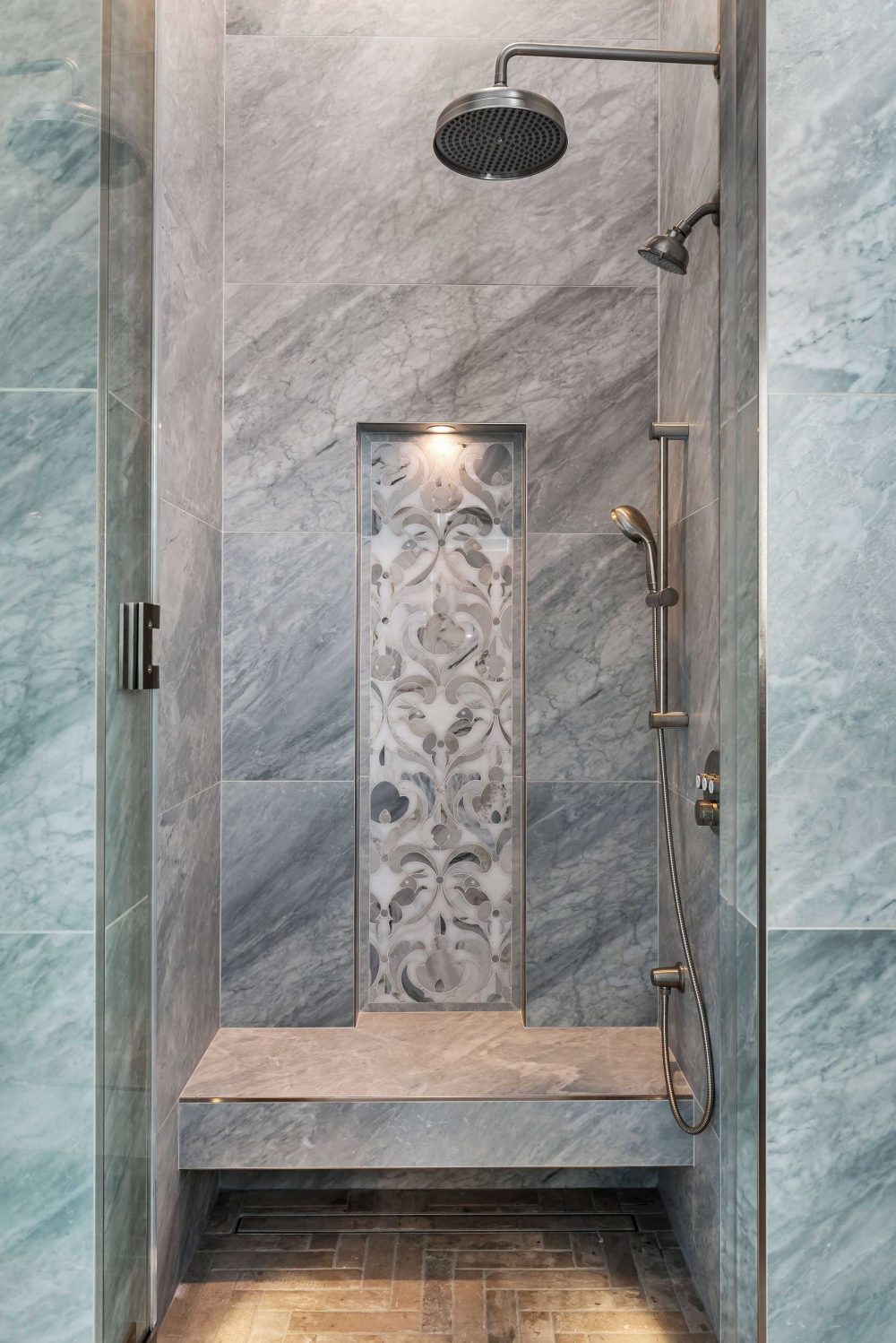 View of walk-in shower stall. Four different stone materials. Built-in bench with white and grey floral inlay design
