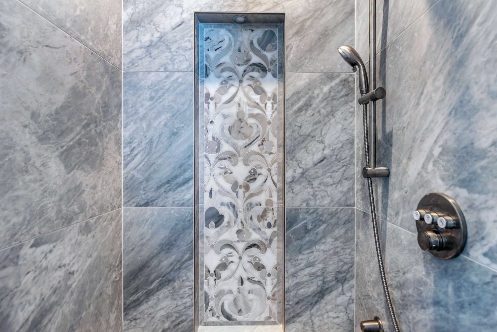 Custom design shower made from grey marbled stone with grey and white floral inlay on one wall