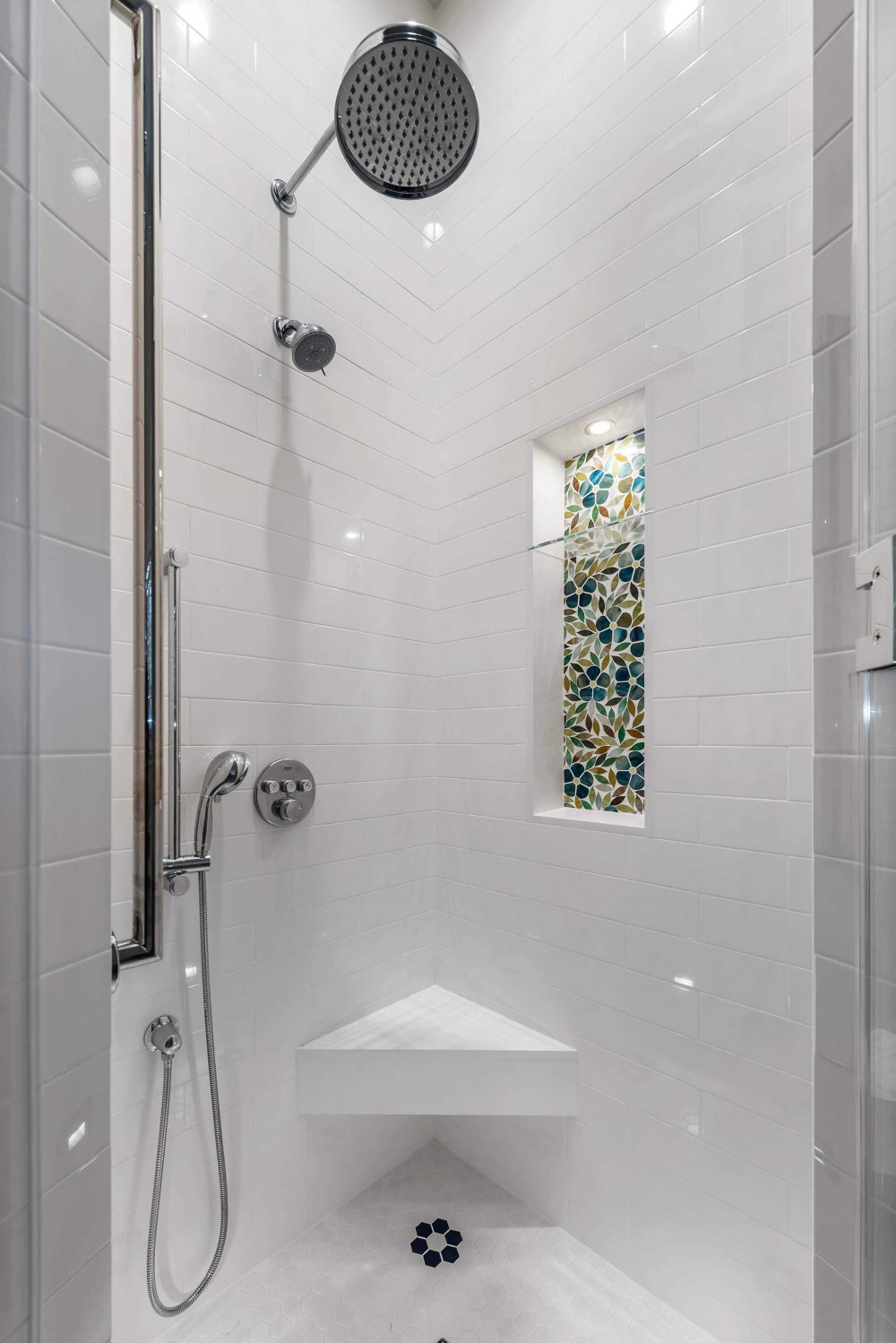 Close up of white tiled walk-in shower with built-in seat and niche with colorful stained-glass
