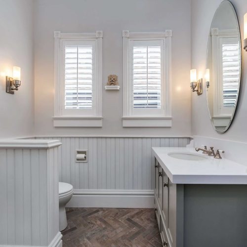 Entry view of bathroom. White wainscoting, hidden toilet, single sink vanity with storage. Earth tones stone floor
