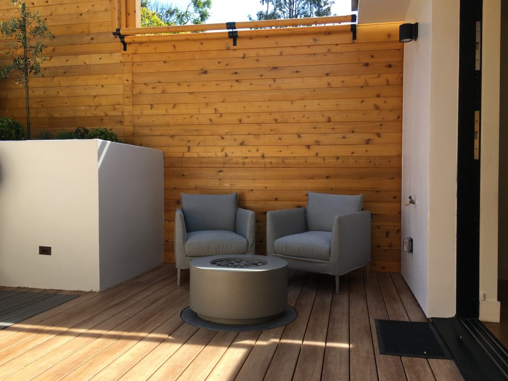 Modern circular smooth grey concrete fire pit with two grey cushioned chairs; large, tall, white square concrete planter