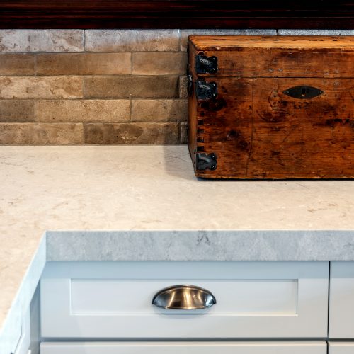Close up of kitchen cabinet pulls, white marble countertop, stone backsplash, dark wood molding