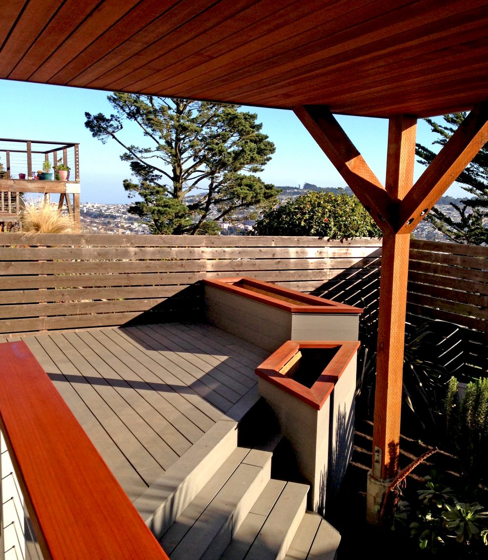 Small elevated deck with a built-in bench and two large, tall trapezoid-shaped planters in place of guard rails underneath a large deck