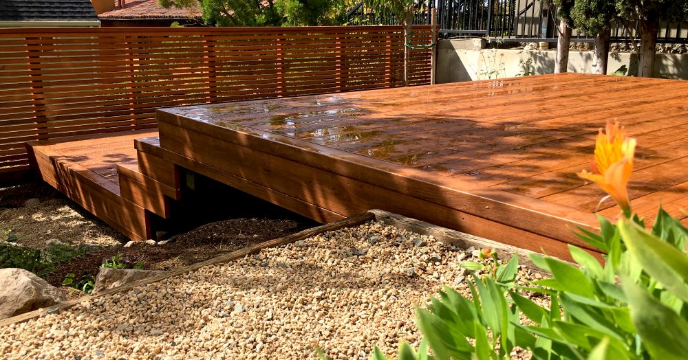 Large multi-level redwood deck stepping down to slatted fence surrounded by pea gravel and plants