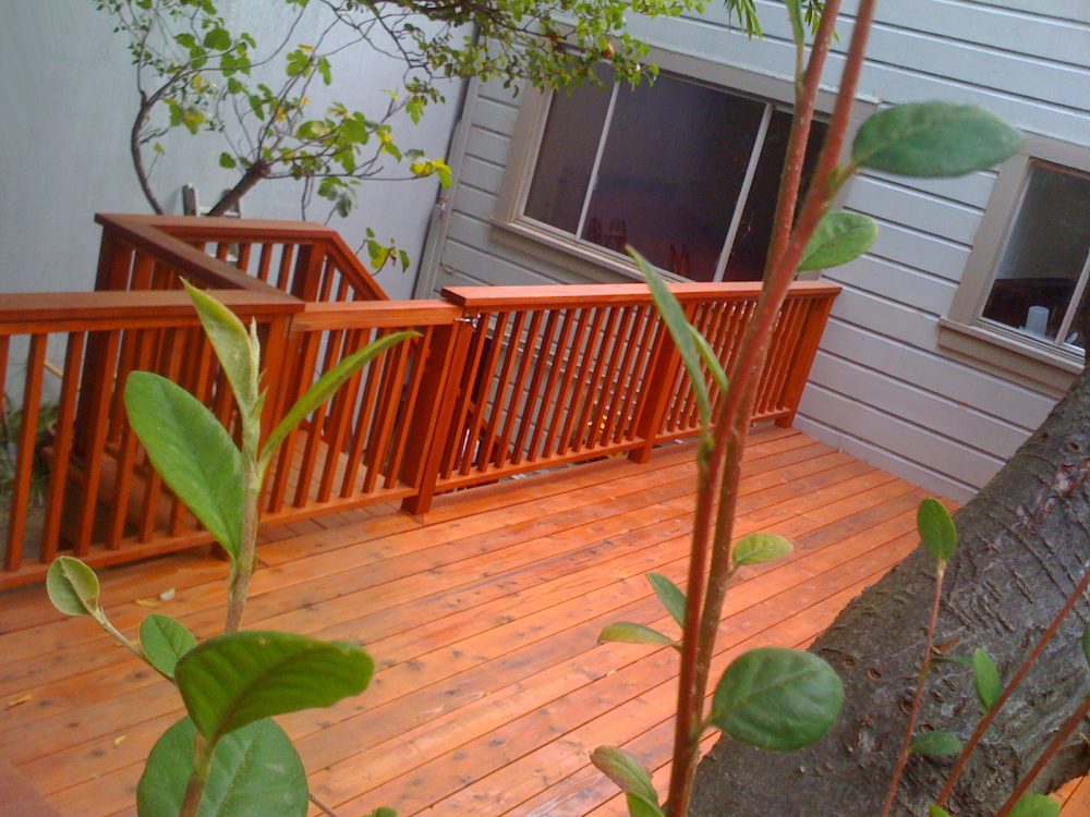 Redwood deck up in the trees on the side of a house with a closed gate leading to steps to go downstairs