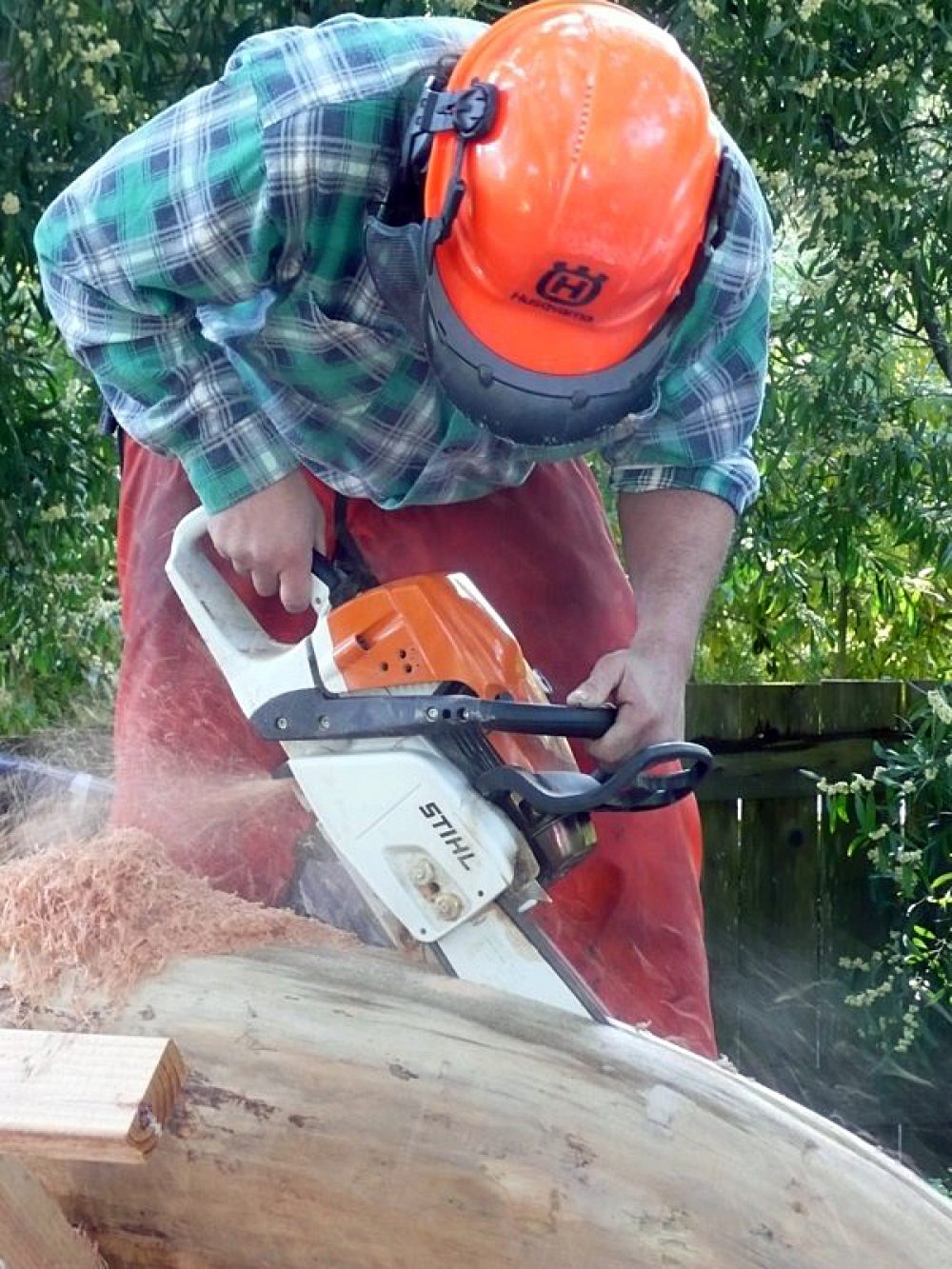 Close up of man in orange hard hat cutting a smooth light colored drift wood log in half