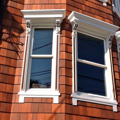 Exterior windows with beautiful detailed molding painted in white on a brown shingled house