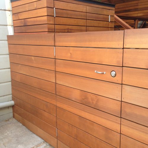 Clean redwood colored wide slat fence with door leading to matching storage