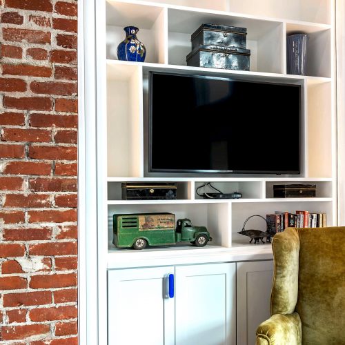 Built in entertainment center with four shelves, two for television and DVD player, and under-cabinets in corner next to brick wall
