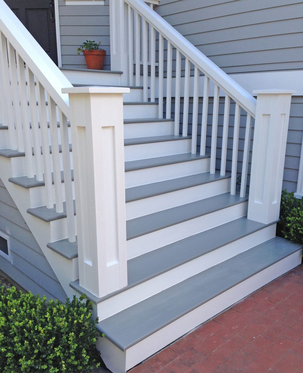 Side view of 10 wooden steps painted white and grey with heavy posts and vertical wood slats leading up to the front door