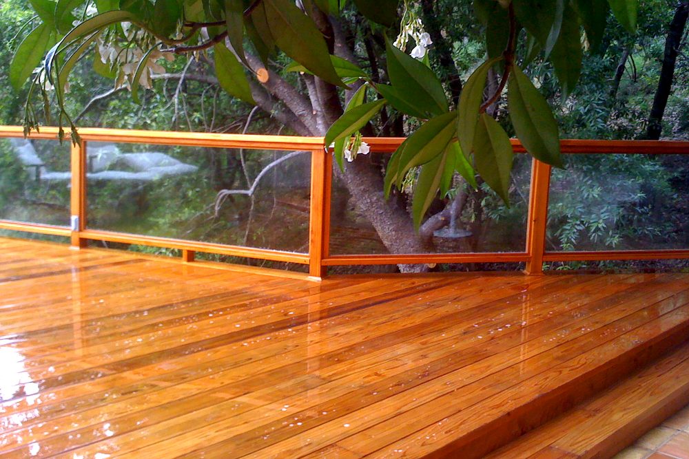 Large wooden deck with clear deck railing right next to trees