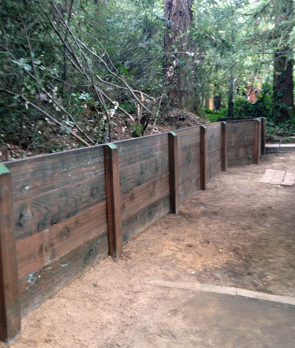 Four-slat wood retaining wall against heavily forested slope