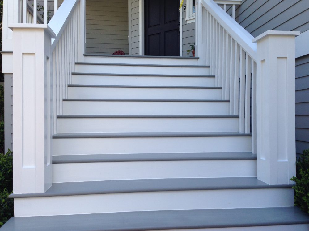 10 wooden steps painted white and grey with heavy posts and vertical wood slats leading up to the front door